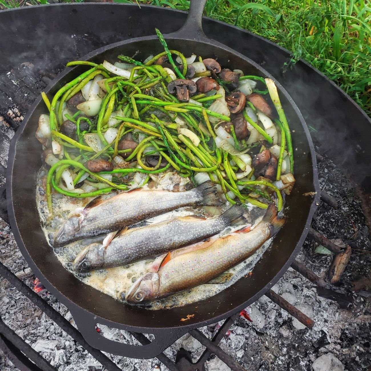 Fish and vegetables frying in a cast iron pan over an open flame